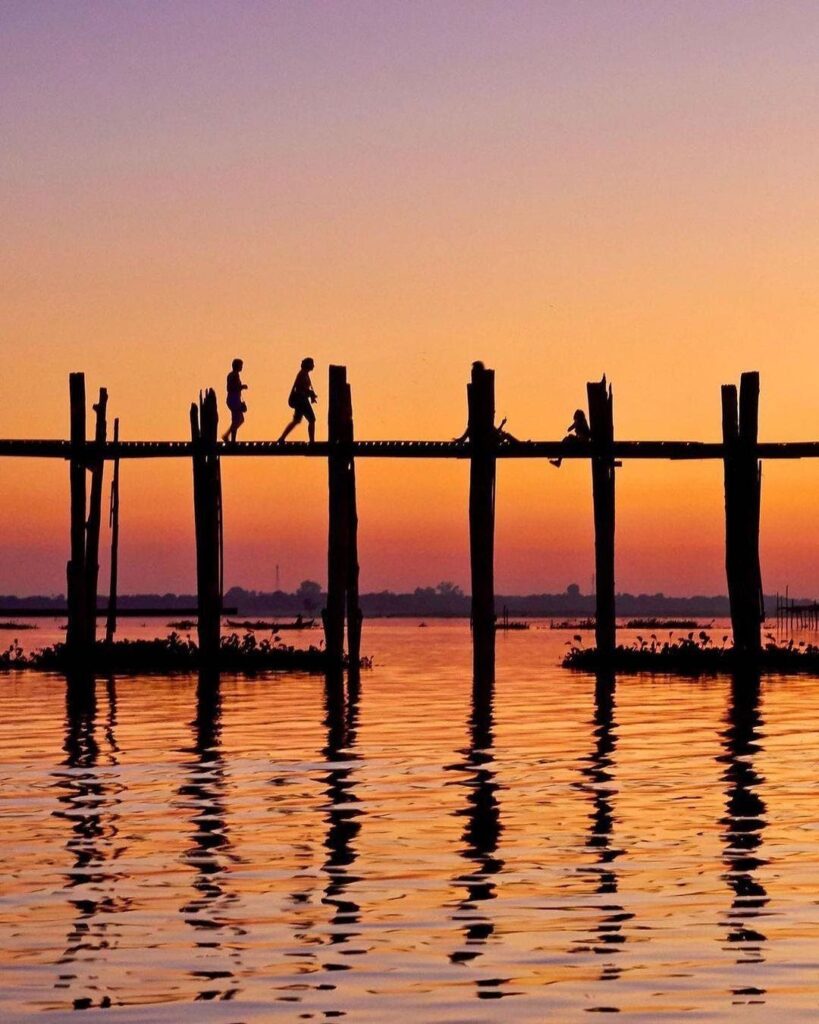 U Bein Bridge creates a striking contrast to the vibrant sunset that draws people to its planks.